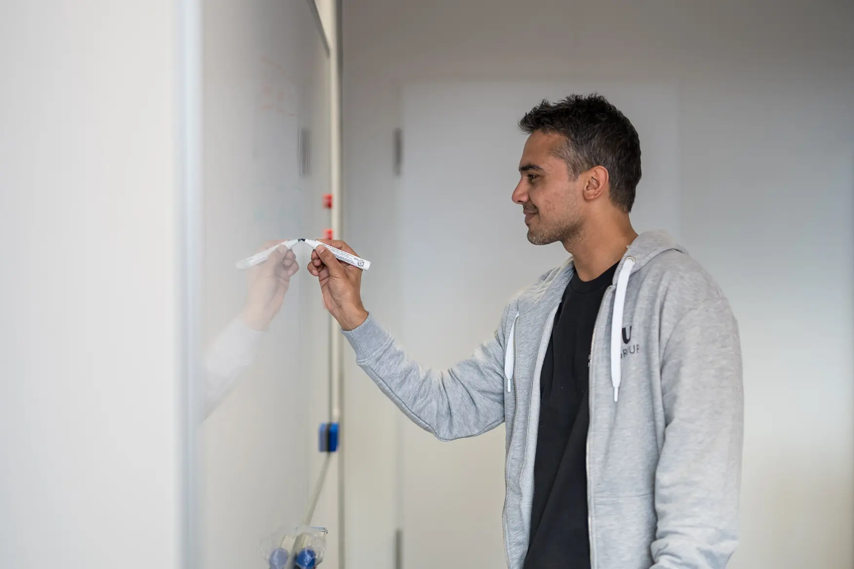 A man from the IT department is standing in front of a whiteboard, smiling as he writes something on it.